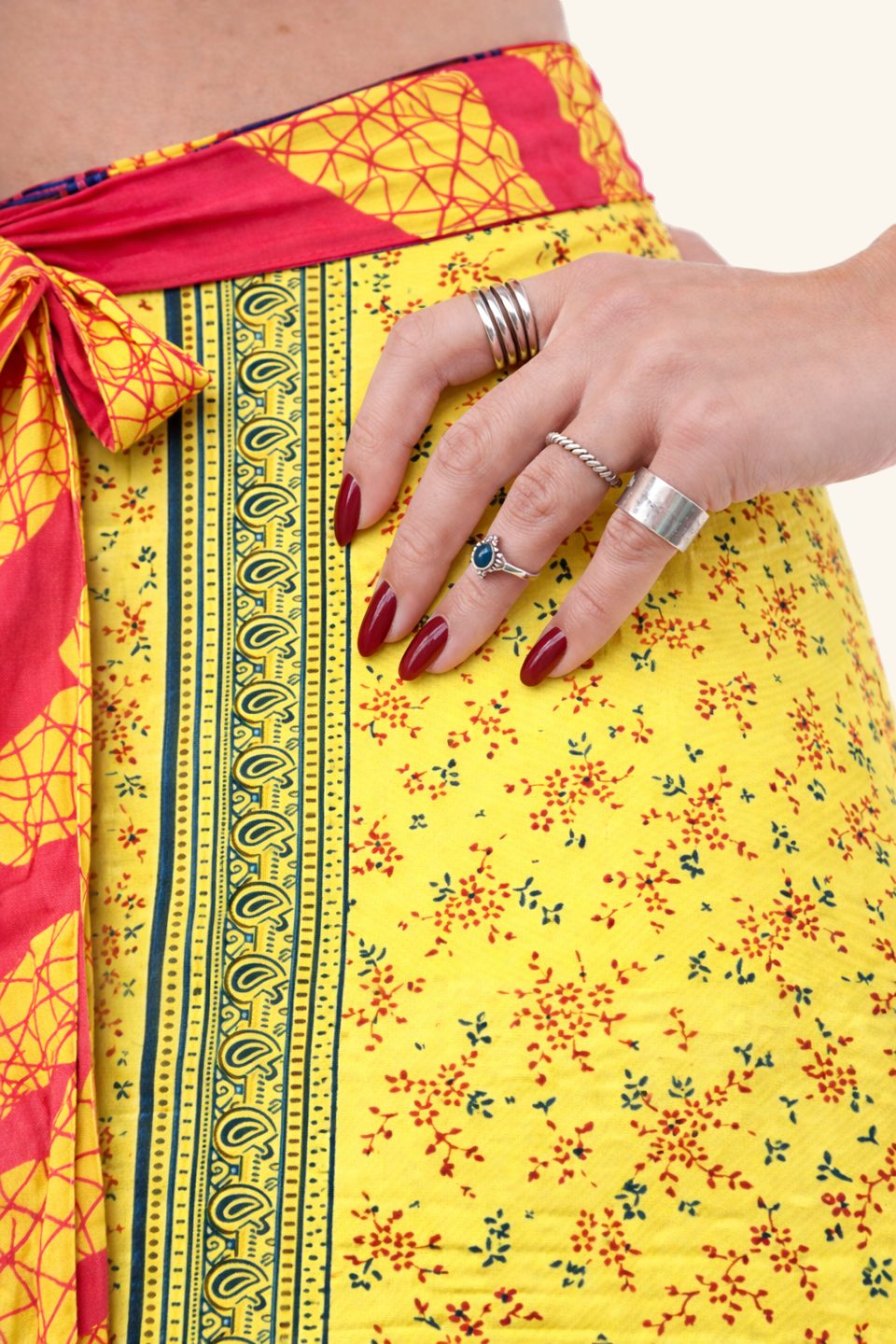 Yellow floral skirt with red and blue accents, worn by a person with silver rings on fingers.