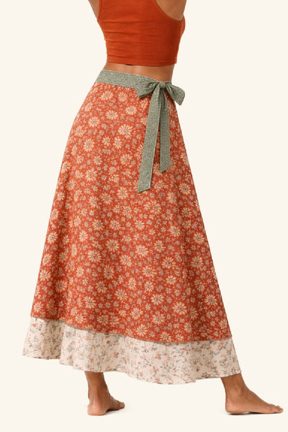 Person wearing a long floral skirt with a rust-colored top on a white background