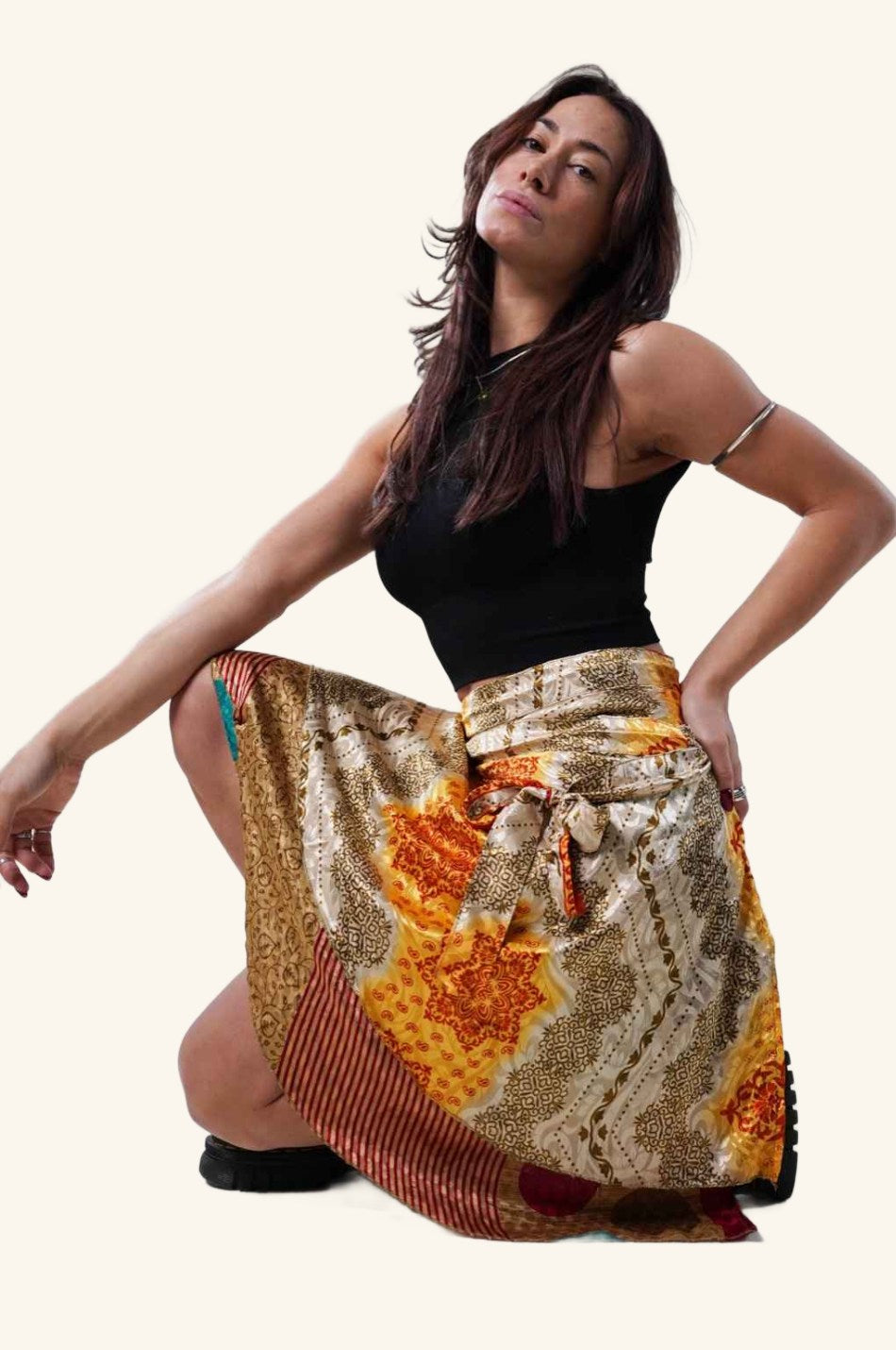Model sitting down and wearing short wrap skirt with golden and orange patterns